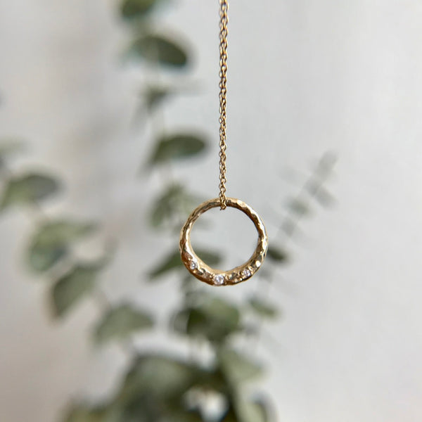 Crescent Moon full circle necklace with white diamonds in the forefront. Eucalyptus in the background.