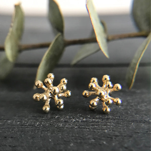 Medium gold dandelion flower earrings on a black wood background with eucalyptus.