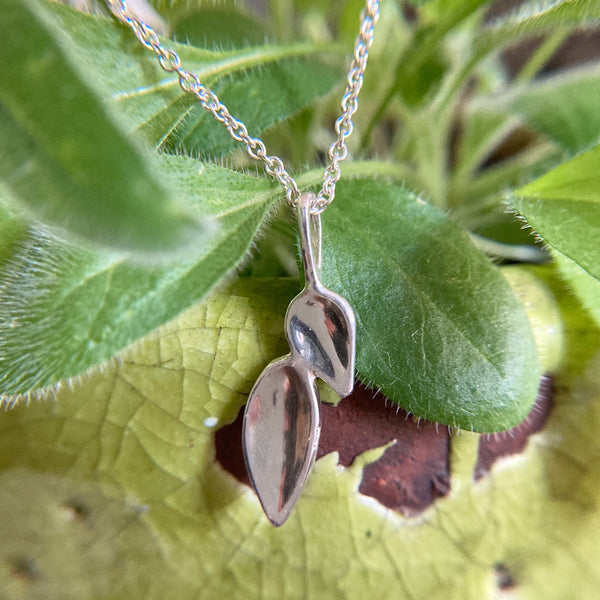 Silver chain with double leaf silver pendant shown hanging from leaves in a flower pot.